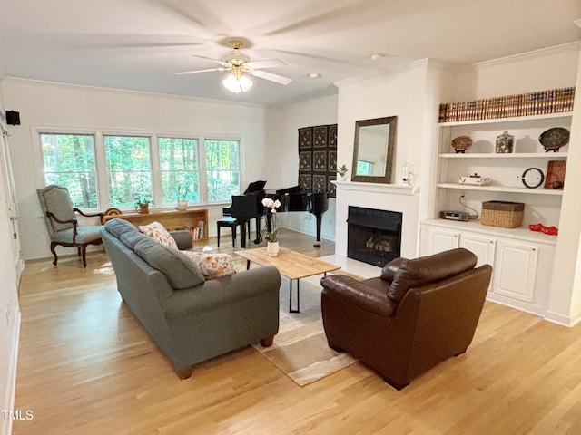 living area with crown molding, ceiling fan, a fireplace, light wood-style flooring, and built in shelves