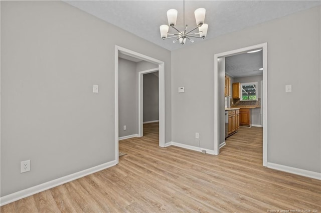 empty room with a chandelier, light wood-style floors, and baseboards
