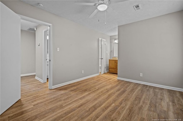 unfurnished bedroom with light wood-style flooring, baseboards, a textured ceiling, ensuite bath, and a ceiling fan