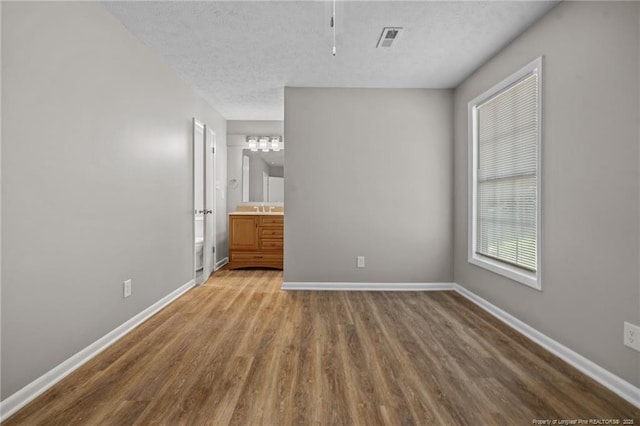 unfurnished bedroom featuring wood finished floors, baseboards, a textured ceiling, a sink, and ensuite bath