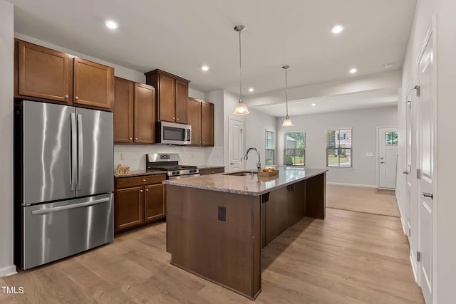 1745 Ripley Woods St, Wake Forest, NC 27587 - kitchen featuring stainless steel appliances, dark stone counters, light wood-type flooring, an island with sink, and decorative light fixtures