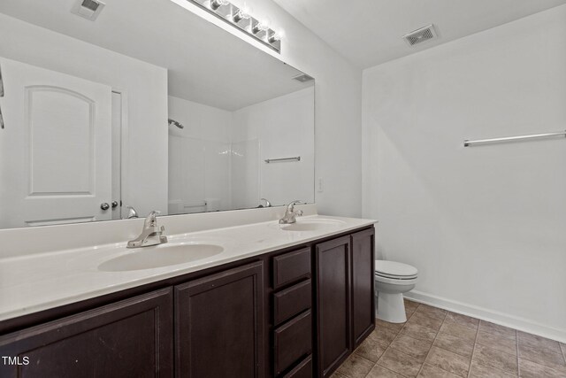 full bathroom featuring toilet, baseboards, a shower, and double vanity