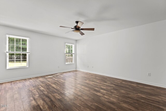 empty room featuring plenty of natural light, dark wood-style floors, a ceiling fan, and baseboards