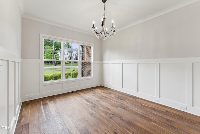 unfurnished room featuring a decorative wall, a chandelier, wood finished floors, crown molding, and a wainscoted wall