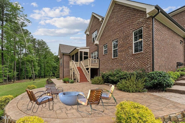 back of property featuring stairway, brick siding, an outdoor fire pit, a patio area, and a sunroom