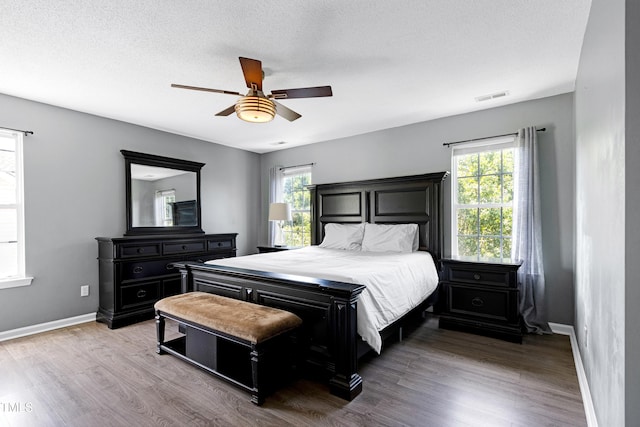 bedroom featuring multiple windows, baseboards, wood finished floors, and ceiling fan