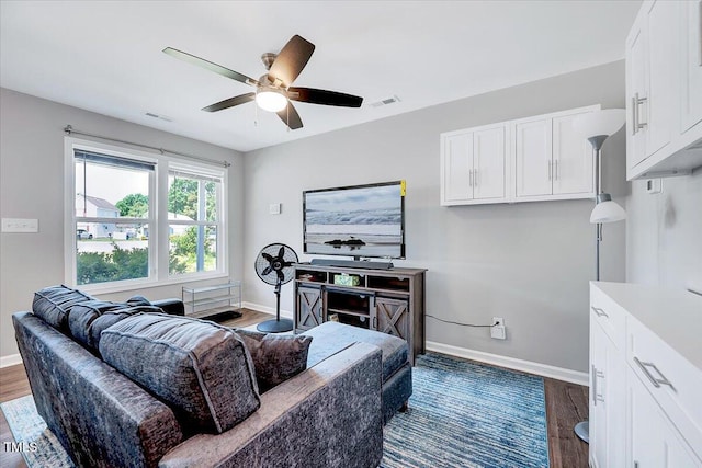 living area with baseboards, a ceiling fan, and dark wood-type flooring