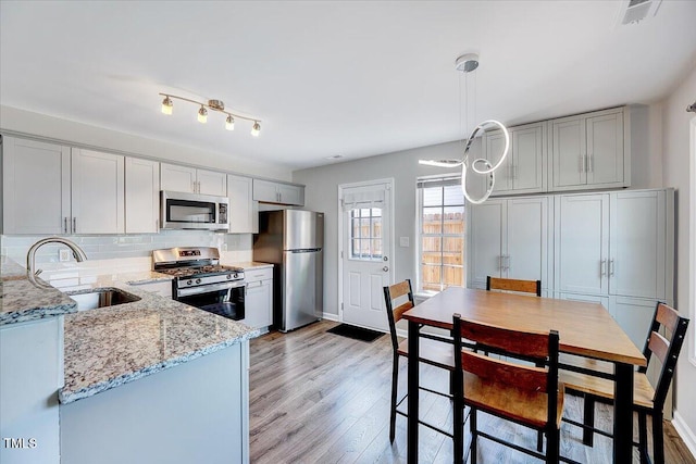 kitchen with appliances with stainless steel finishes, a sink, light wood finished floors, light stone countertops, and backsplash