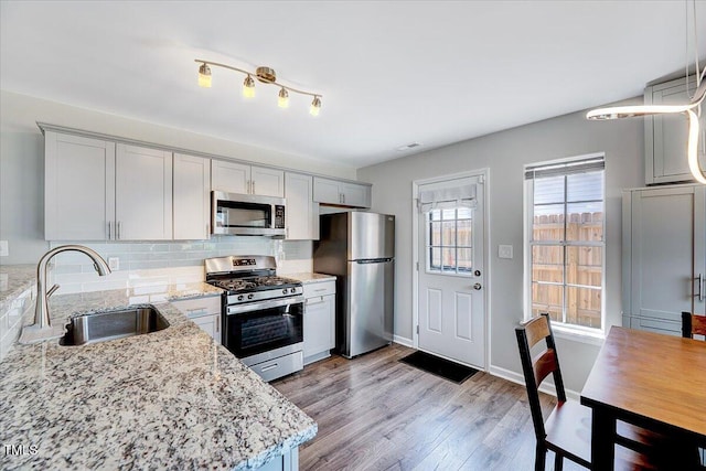 kitchen featuring stainless steel appliances, a sink, light stone counters, decorative backsplash, and light wood-type flooring