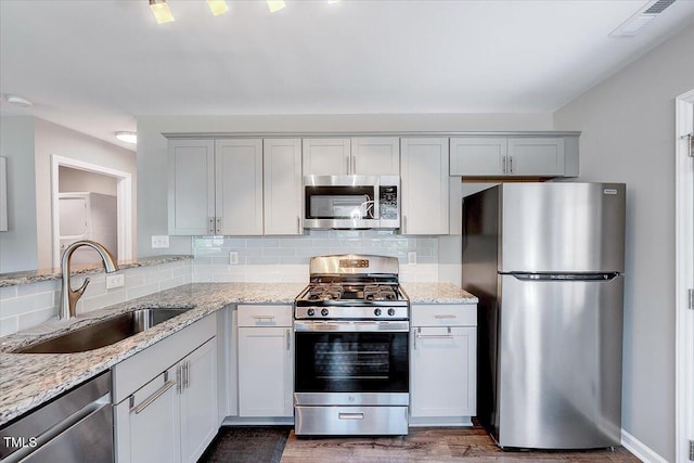 kitchen featuring stainless steel appliances, a sink, wood finished floors, tasteful backsplash, and light stone counters