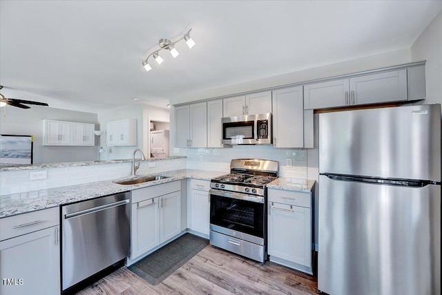 kitchen with appliances with stainless steel finishes, a sink, a ceiling fan, light stone counters, and decorative backsplash