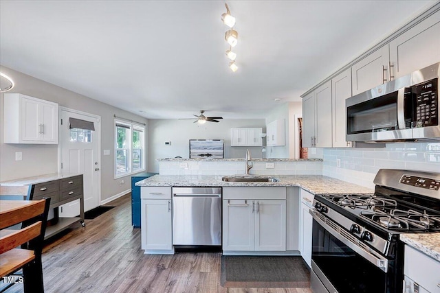 kitchen with appliances with stainless steel finishes, a sink, a peninsula, a ceiling fan, and light wood-type flooring