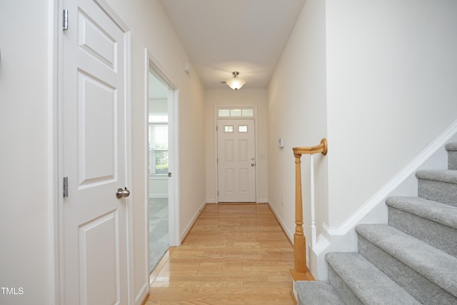 entryway with light wood-type flooring, stairway, and baseboards