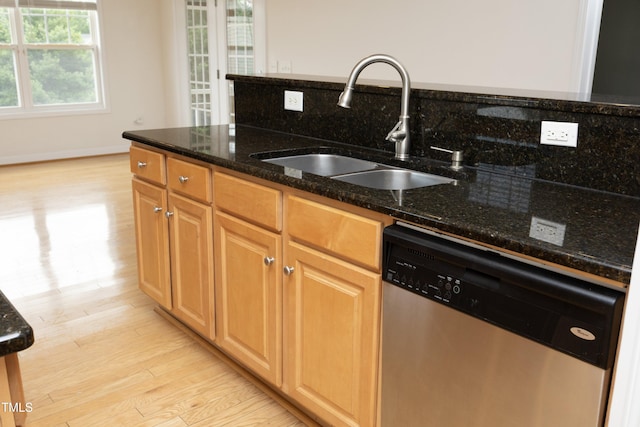 kitchen featuring stainless steel dishwasher, a sink, light wood finished floors, dark stone counters, and baseboards
