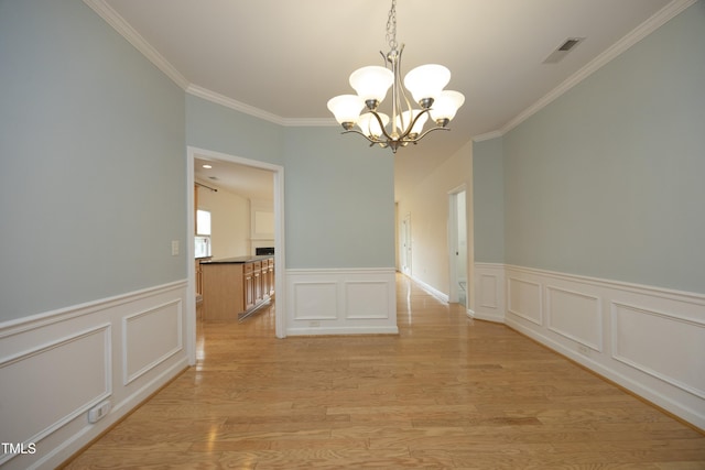unfurnished dining area featuring crown molding, a chandelier, light wood-style floors, a wainscoted wall, and a decorative wall