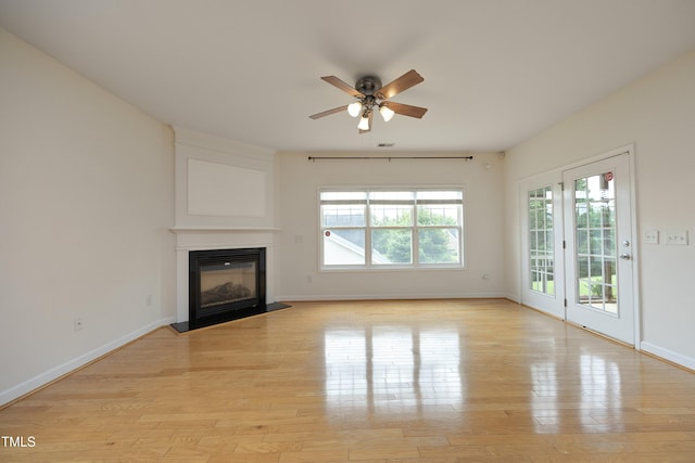 unfurnished living room with ceiling fan, light wood-style floors, a fireplace with flush hearth, and baseboards