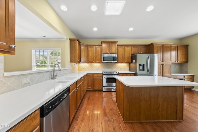 kitchen with appliances with stainless steel finishes, a sink, a kitchen island, brown cabinets, and recessed lighting