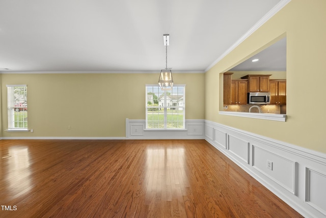 unfurnished dining area featuring wood finished floors, plenty of natural light, a wainscoted wall, crown molding, and a chandelier