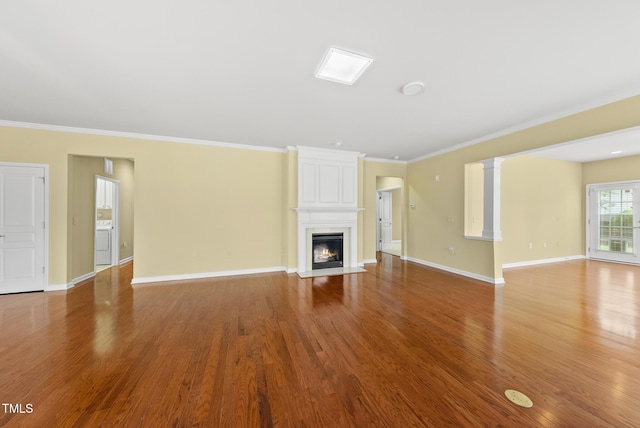 unfurnished living room featuring ornamental molding, washer / dryer, wood finished floors, a large fireplace, and baseboards