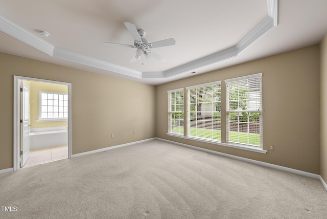 unfurnished room with a raised ceiling, carpet floors, crown molding, baseboards, and ceiling fan