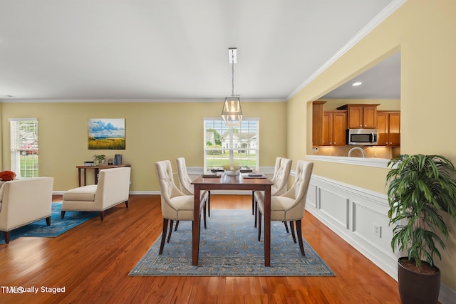 dining space with wood finished floors, healthy amount of natural light, ornamental molding, and a chandelier