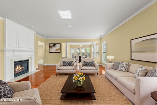 living room featuring light wood-style floors, crown molding, baseboards, and a large fireplace