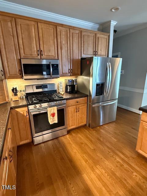 kitchen with stainless steel appliances, ornamental molding, wood finished floors, decorative backsplash, and brown cabinetry