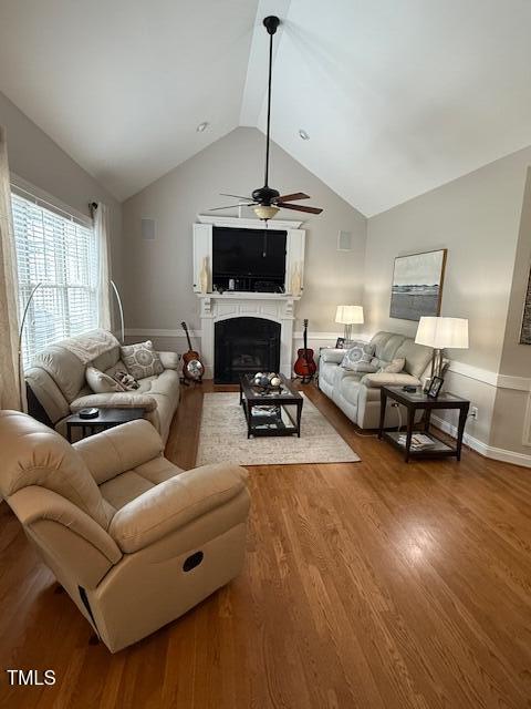 living area featuring ceiling fan, a fireplace, vaulted ceiling, and wood finished floors
