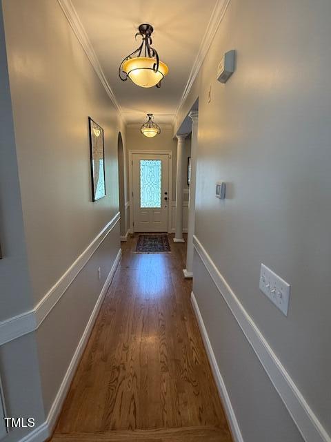 doorway to outside with wood finished floors, crown molding, arched walkways, and baseboards