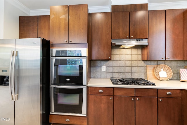 kitchen featuring appliances with stainless steel finishes, under cabinet range hood, light countertops, tasteful backsplash, and ornamental molding