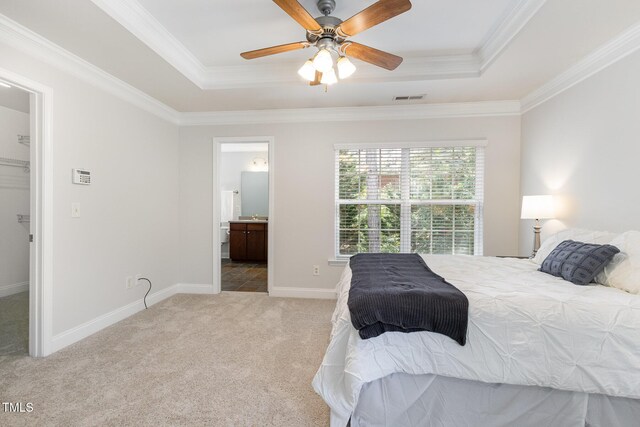 carpeted bedroom featuring a raised ceiling, ornamental molding, baseboards, ensuite bathroom, and a ceiling fan