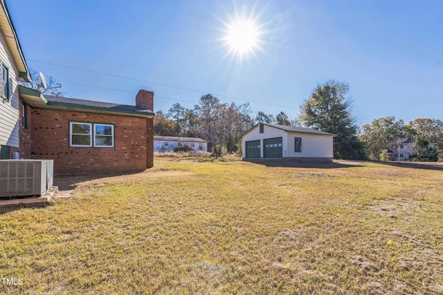 view of grassy yard with central air condition unit, a detached garage, and an outdoor structure