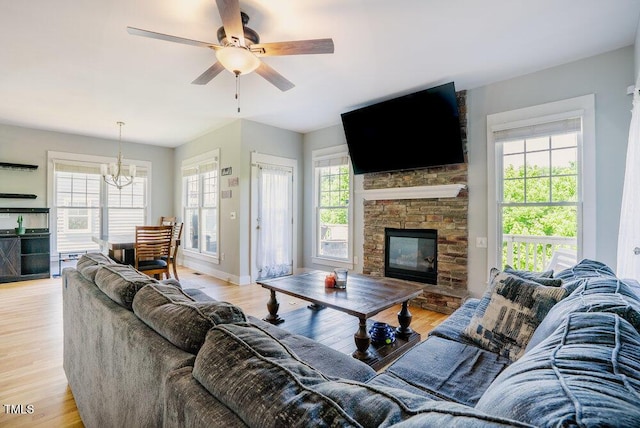 living room featuring a chandelier, light wood-style floors, a ceiling fan, and a stone fireplace