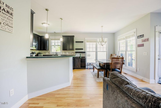 kitchen featuring a chandelier, light wood finished floors, a sink, baseboards, and stainless steel microwave