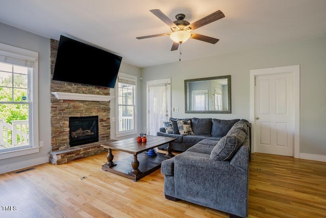 living area featuring baseboards, wood finished floors, ceiling fan, and a stone fireplace