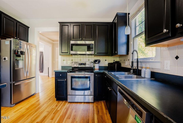 kitchen with stainless steel appliances, a sink, dark countertops, light wood-style floors, and healthy amount of natural light