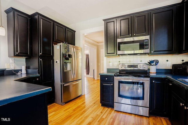 kitchen featuring appliances with stainless steel finishes, dark countertops, light wood-style floors, tasteful backsplash, and dark cabinetry