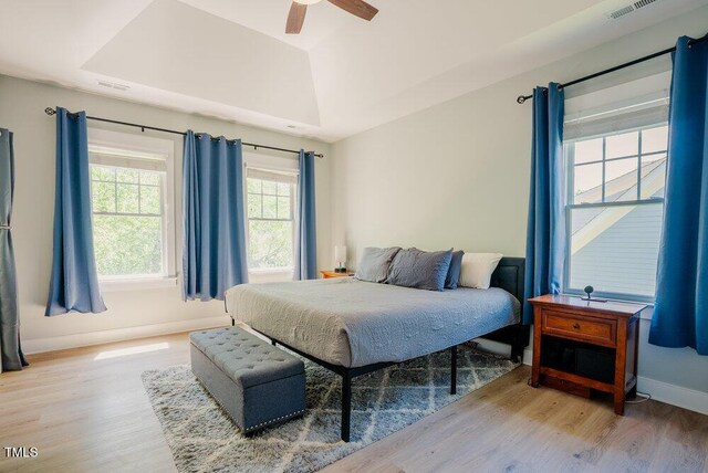 bedroom featuring wood finished floors, baseboards, a raised ceiling, and a ceiling fan
