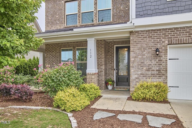 entrance to property featuring brick siding, a garage, and covered porch