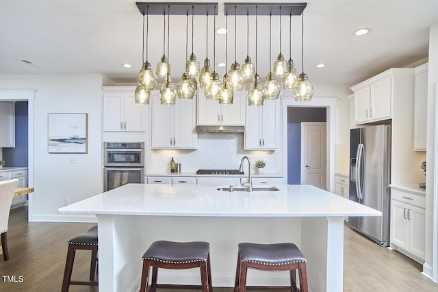 kitchen featuring a sink, appliances with stainless steel finishes, a kitchen breakfast bar, under cabinet range hood, and light wood finished floors