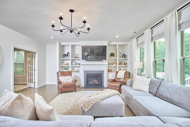 living area featuring a chandelier, wood finished floors, a fireplace with flush hearth, baseboards, and recessed lighting