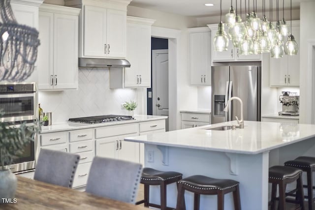 kitchen with appliances with stainless steel finishes, a sink, under cabinet range hood, tasteful backsplash, and a breakfast bar area