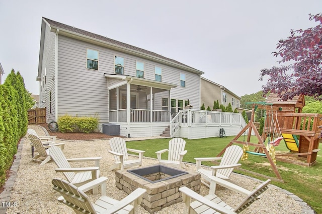 rear view of property featuring a fire pit, a sunroom, a playground, ceiling fan, and a deck