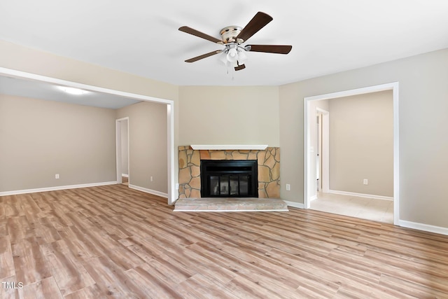 unfurnished living room featuring wood finished floors, ceiling fan, a fireplace, and baseboards