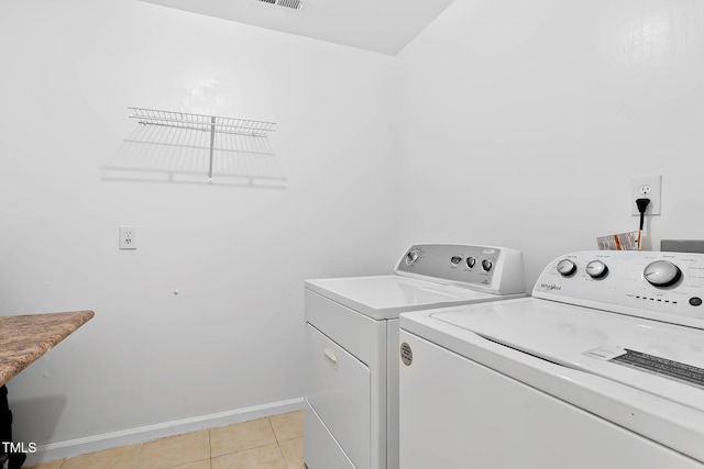 clothes washing area with washer and clothes dryer, light tile patterned floors, and baseboards