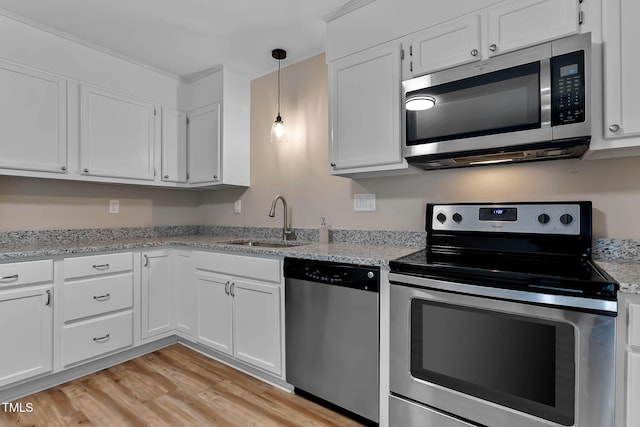 kitchen featuring appliances with stainless steel finishes, a sink, light wood-style flooring, white cabinetry, and hanging light fixtures