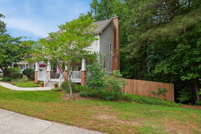 view of property hidden behind natural elements featuring a chimney and a porch