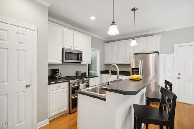 kitchen with appliances with stainless steel finishes, dark countertops, a sink, crown molding, and white cabinetry
