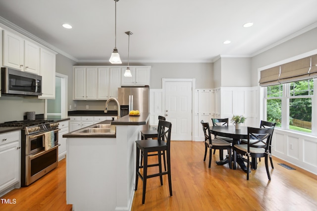 kitchen with stainless steel appliances, a sink, dark countertops, white cabinets, and crown molding