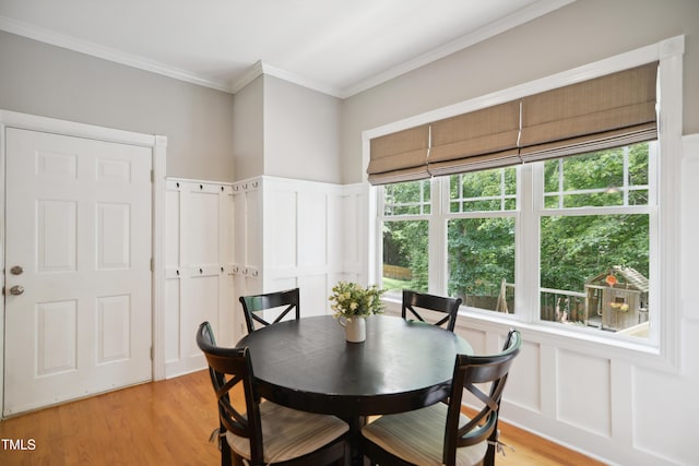 dining space with a decorative wall, ornamental molding, light wood-style floors, and wainscoting